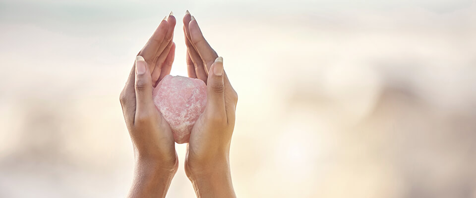 Frauenhände mit einem rosa Edelstein in der Hand