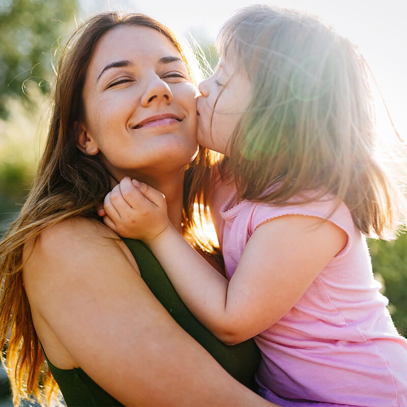 Kleines Mädchen küsst Mutter im Sonnenlicht